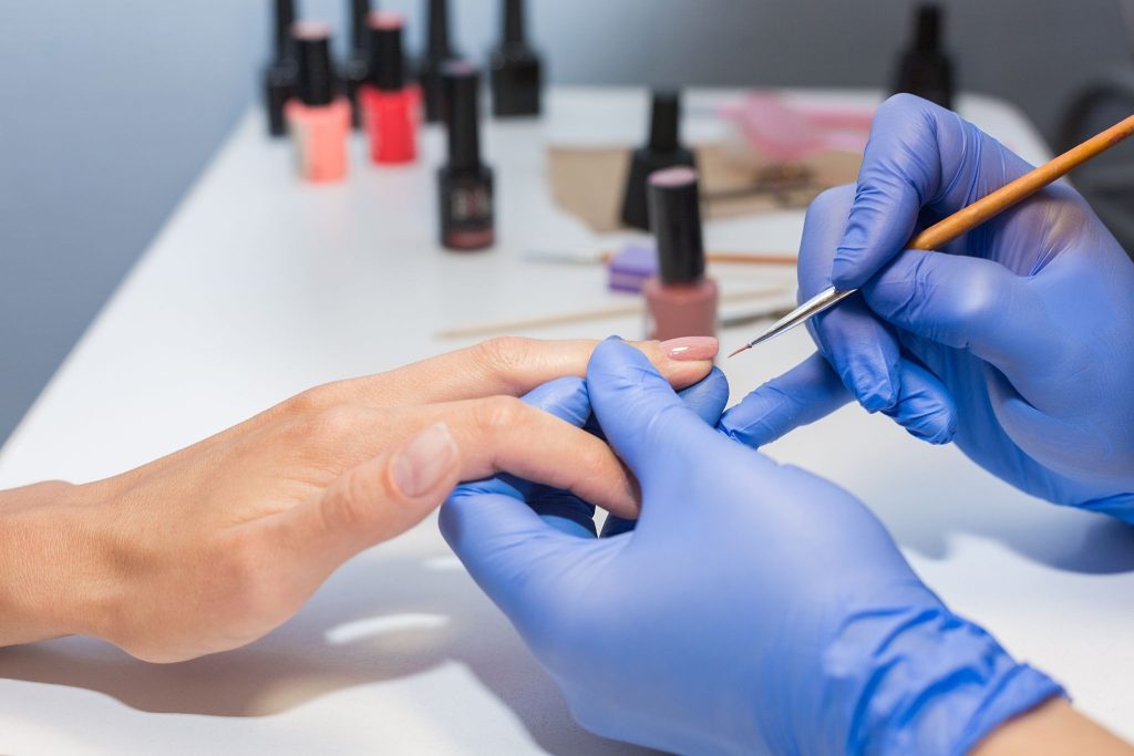 Professional manicurist wearing gloves, carefully applying nail polish during a manicure treatment.